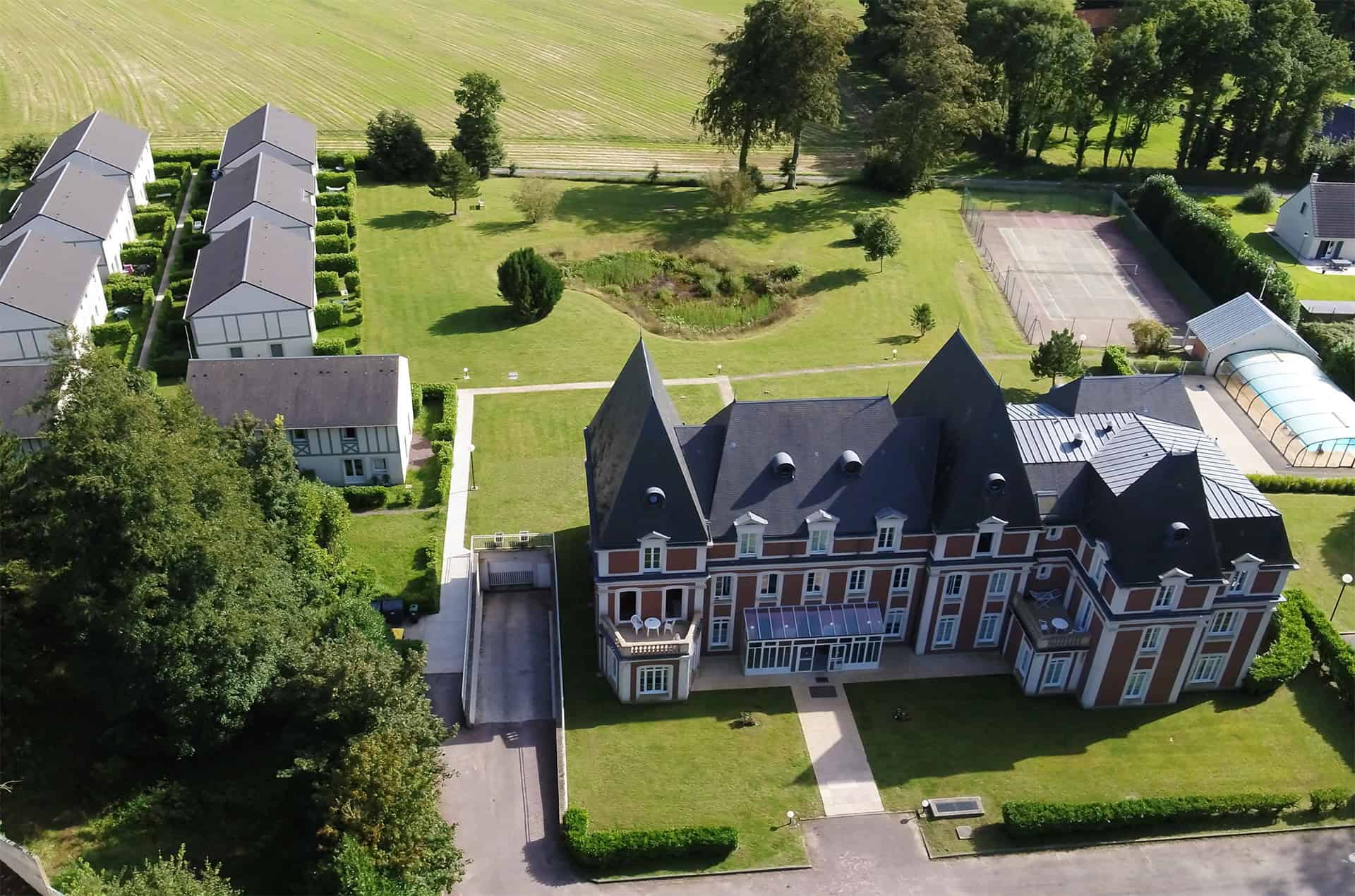 Vue aérienne du château, des cottages (à gauche) et de la piscine extérieure couverte (à droite) de la résidence de vacances Goélia Les Portes d'Etretat à proximité d'Etretat en Normandie Vue aérienne du château, des cottages (à gauche) et de la piscine extérieure couverte (à droite) de la résidence de vacances Goélia Les Portes d'Etretat à proximité d'Etretat en Normandie